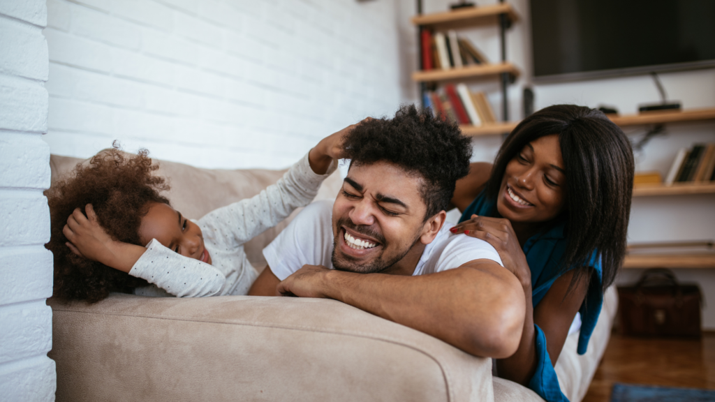 Family of a mother, father and child playfully laugh together on a couch.